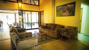 Um hall espaçoso com teto alto, um amplo sofá, uma mesa de centro e uma pintura da Serra do Roncador.