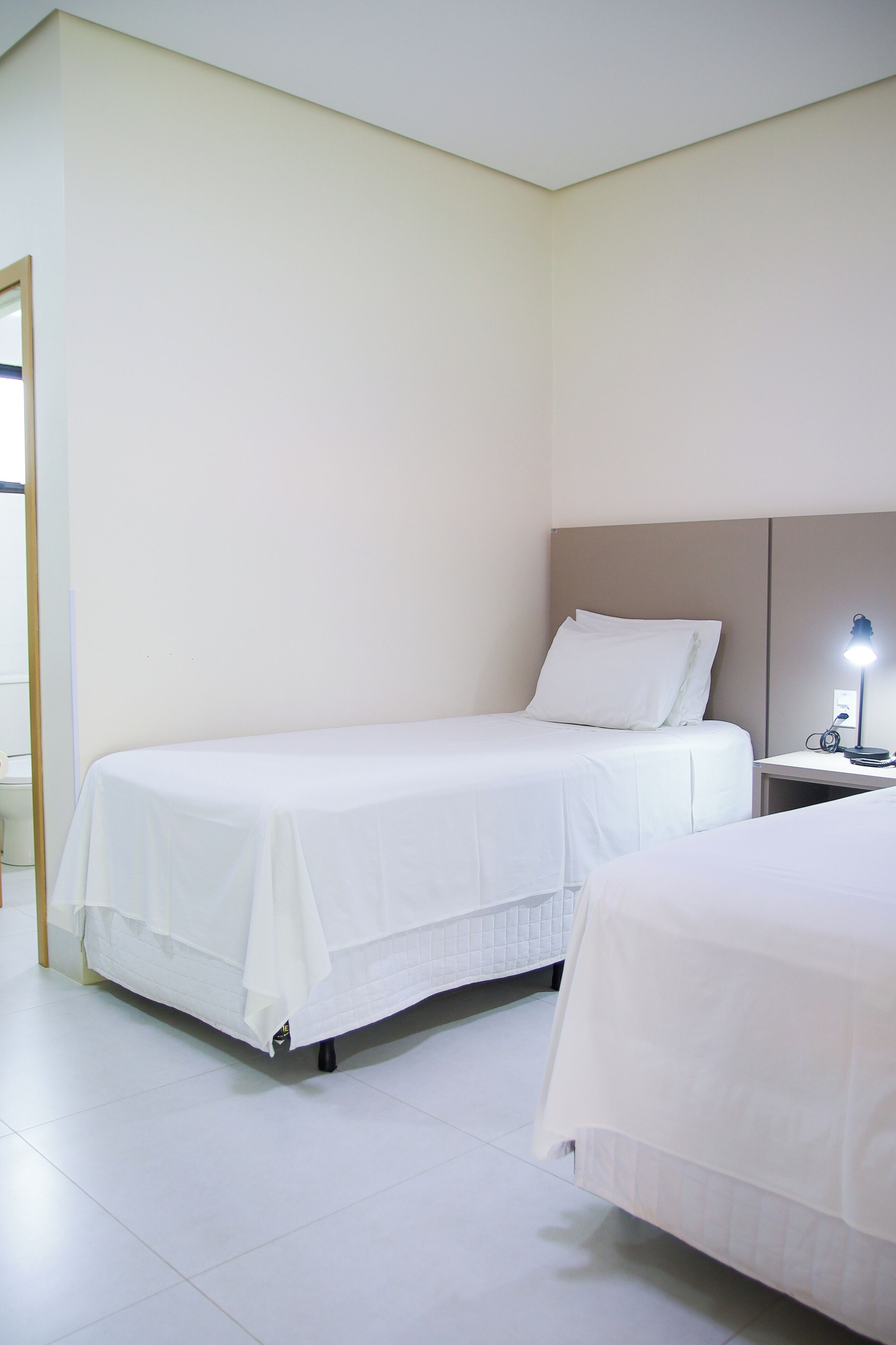 Una camera d'albergo con due letti singoli, un comodino con una lampada e una parete spoglia.