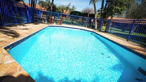 Piscina retangular com borda azulejada, rodeada por uma cerca de metal azul e um deck de pedra.
