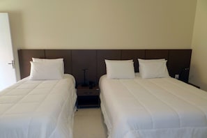Two single beds with white duvets, a nightstand with a lamp and telephone, and a dark wood headboard.