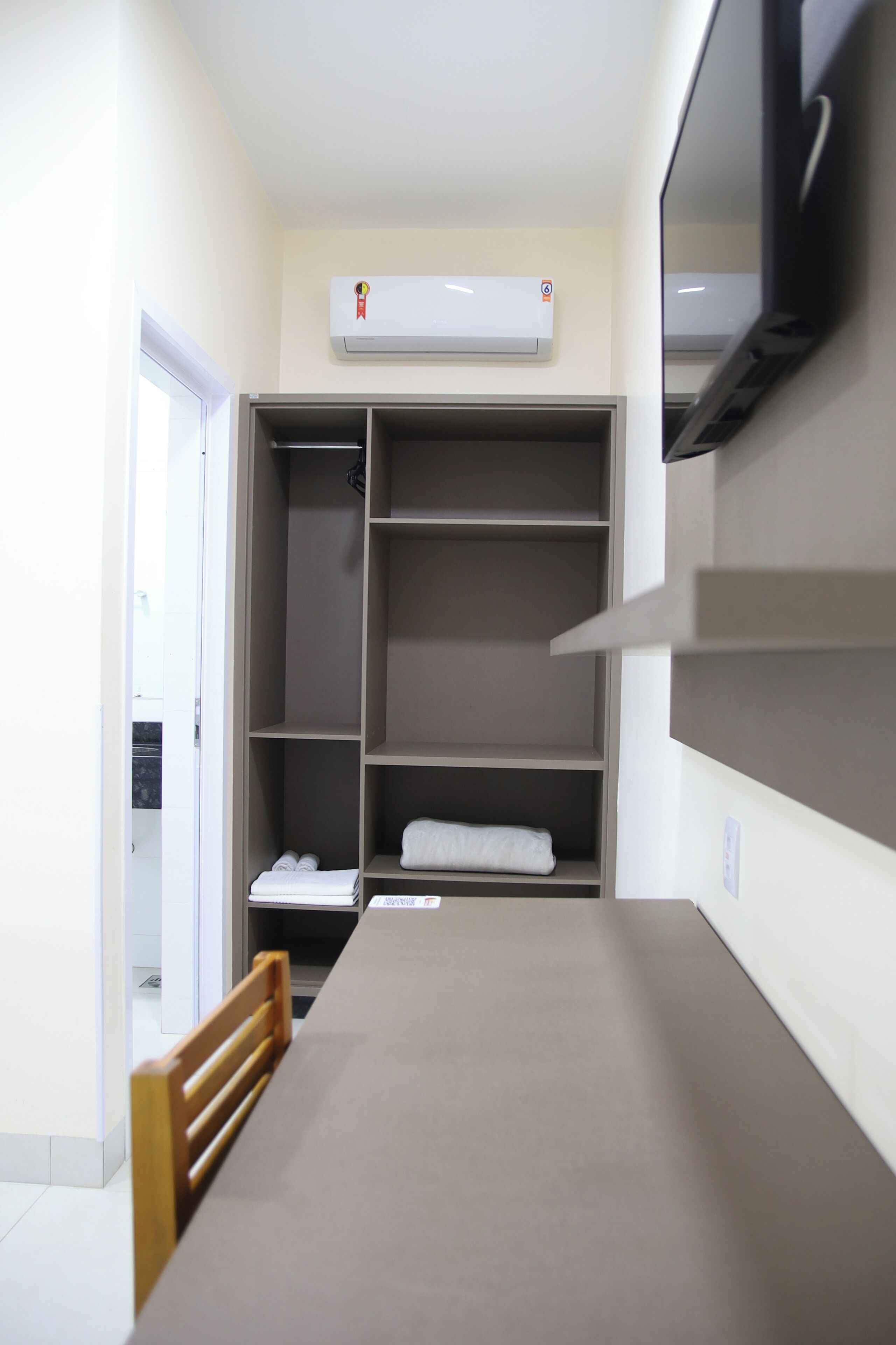A room with a bed, a wooden chair, a wardrobe, and an air conditioning unit.