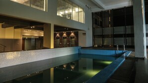 Una piscina interior con suelo de baldosas, una escalera y un muro de cristal.