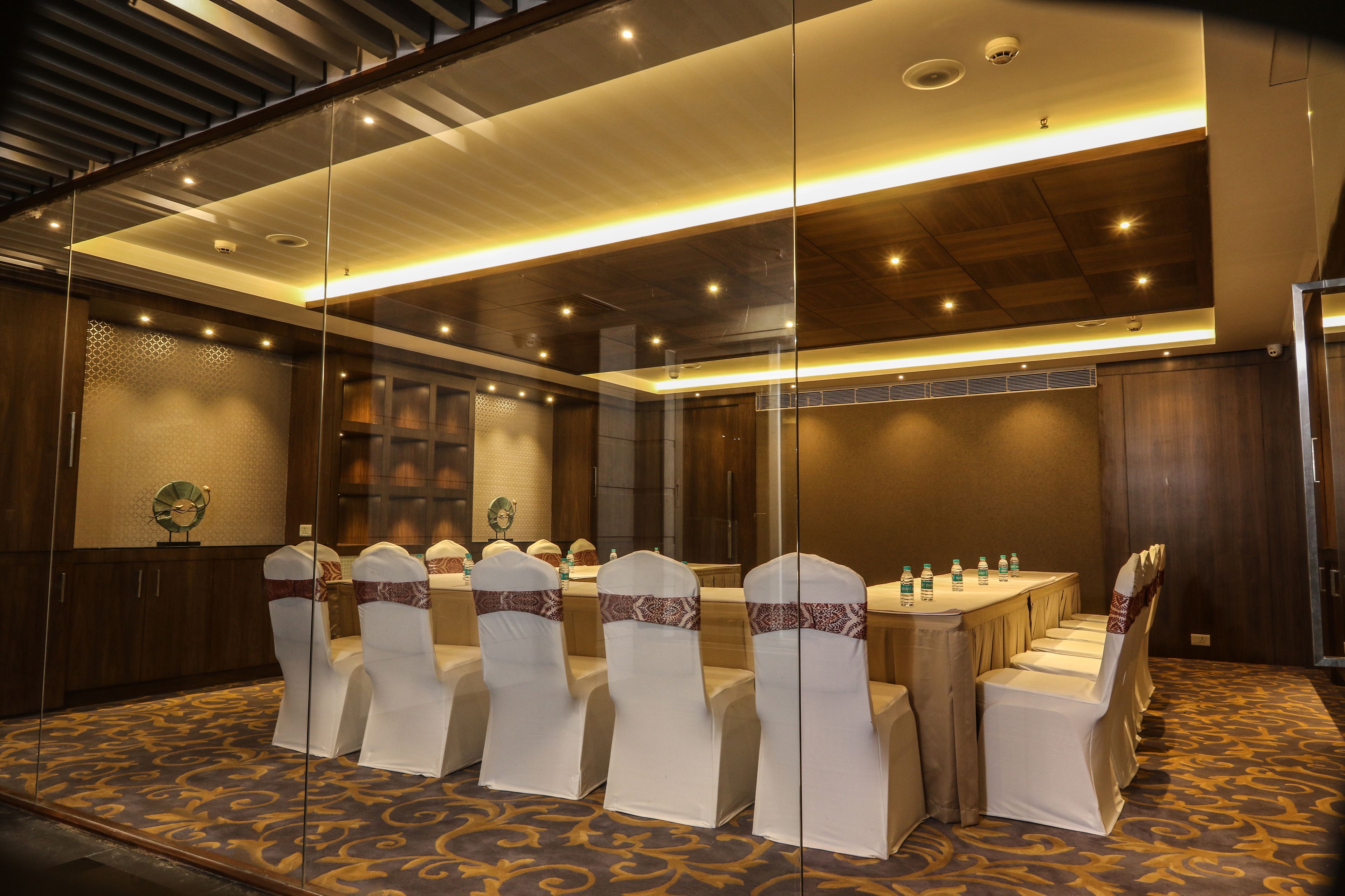A conference room with a long table, chairs with white covers, and a patterned carpet.