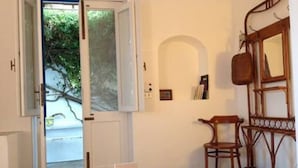 Una stanza con un letto, una sedia, una poltrona in legno dallo schienale curvo, uno specchio e una porta che dà sull'esterno.