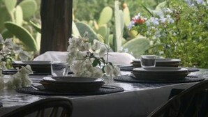 Tavolo apparecchiato all'aperto con piatti, bicchieri e un centrotavola di fiori bianchi.