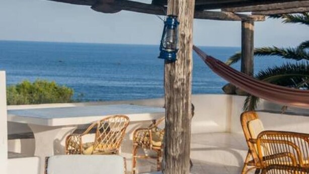 Una terrazza vista mare con sedie in vimini, un'amaca e una lanterna.