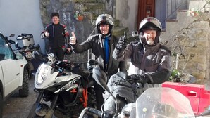 Un grupo de motociclistas posando con sus motos en una zona residencial con edificios de piedra y un buzón a la vista.