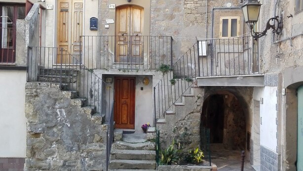 Un patio con edificios de piedra, una puerta de madera y una escalera que sube a un segundo piso.