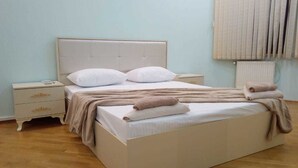 A neatly made bed with a headboard, a bedside table with a lamp, and a window with curtains. - Yeshim Guest House (Baku)