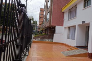 A narrow alleyway with a tiled floor, a black metal fence, and a building with a yellow and white facade. - Hotel Maceo Chico (Bogotá)