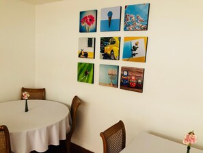 A dining area with a round table and four chairs, a wall with nine artworks, and a vase with flowers on the table. - Hotel Maceo Chico (Bogotá)