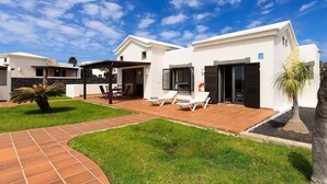 Una casa moderna con un patio, mobiliario de exterior y un césped bien cuidado.