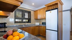Una cocina con encimeras de granito, armarios de madera, un refrigerador blanco y un frutero.