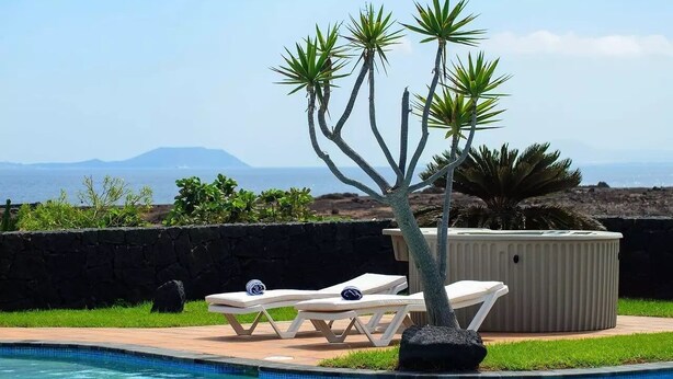 Zona de piscina con sillones de descanso, jacuzzi y vista al océano.
