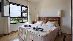 Habitación de hotel con dos camas, un ventanal con vistas a una piscina y palmeras, y cabecero de madera.