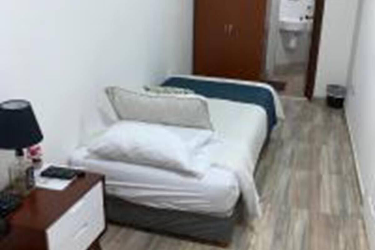 Une petite chambre propre, avec un lit, une table de chevet dotée d’une lampe et une armoire.