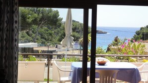 Un balcon avec une table et des chaises, donnant sur un paysage côtier avec des arbres et une vue sur la mer.