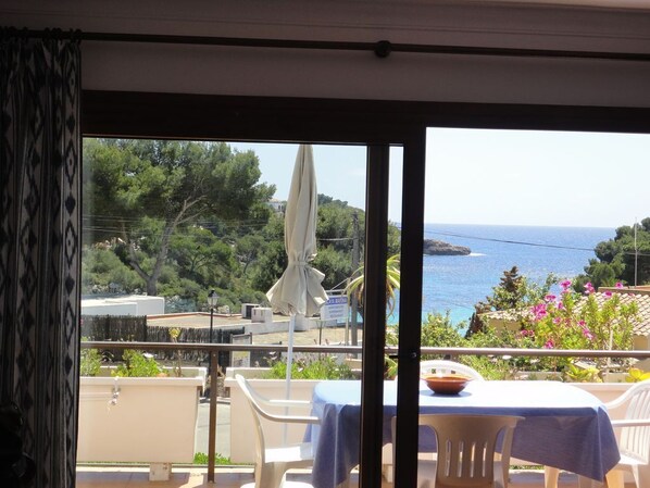 A balcony with a table and chairs, overlooking a coastal view with trees and a body of water.