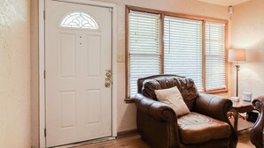 A room with a white door with a stained glass window, a brown leather armchair, and a window with blinds.