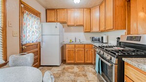 A compact kitchen with wooden cabinets, a white refrigerator, a stove, a microwave, and a sink.