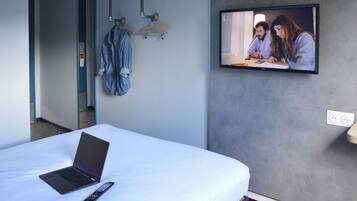 Hotelkamer met een bed, een laptop, een afstandsbediening, een televisie aan de muur en een deur naar een andere kamer.