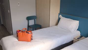 A hotel room with a bed, a chair, a nightstand, and a bag on the bed.