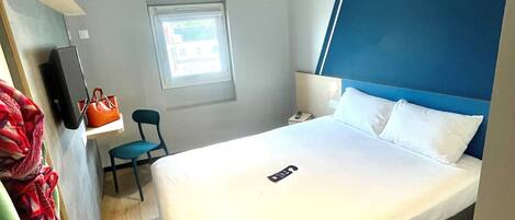 Una habitación de hotel con cama, escritorio, silla, ventana y perchero.