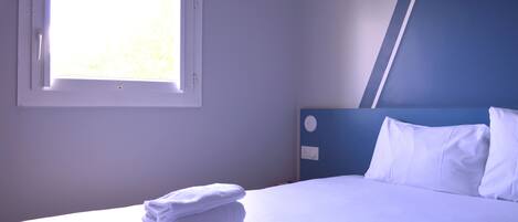 Hotellihuone, jossa on sänky, ikkuna ja sinisellä värillä korostettu seinä.