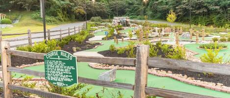 Un campo de mini golf con cerca de madera y un cartel que enumera las normas del juego.