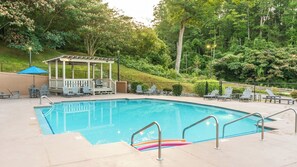 Une piscine rectangulaire dotée d’un espace de détente, entourée de chaises longues et agrémentée d’un gazebo.