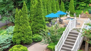 A residential outdoor area with a staircase leading to a deck, surrounded by lush greenery and a swimming pool. - MountainLoft 2 Bedroom 60 day blackout (Gatlinburg)
