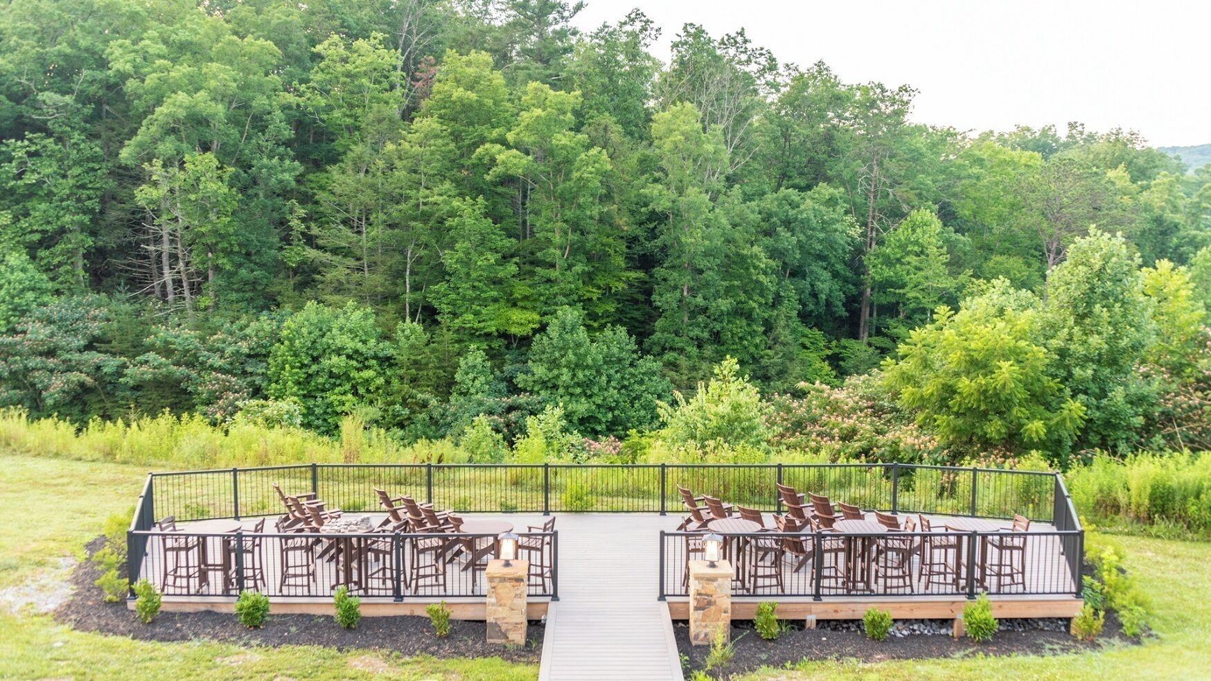 An outdoor deck with seating and a pathway leading to it, surrounded by dense greenery.