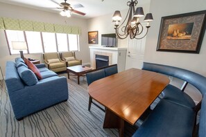 A hotel room with a dining table, blue sofa, two armchairs, a fireplace, and a ceiling fan. - MountainLoft 2 Bedroom 60 day blackout (Gatlinburg)