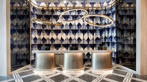 Un espace d’accueil agrémenté d’un mur aux motifs géométriques, d’un lustre moderne et d’un comptoir de réception.