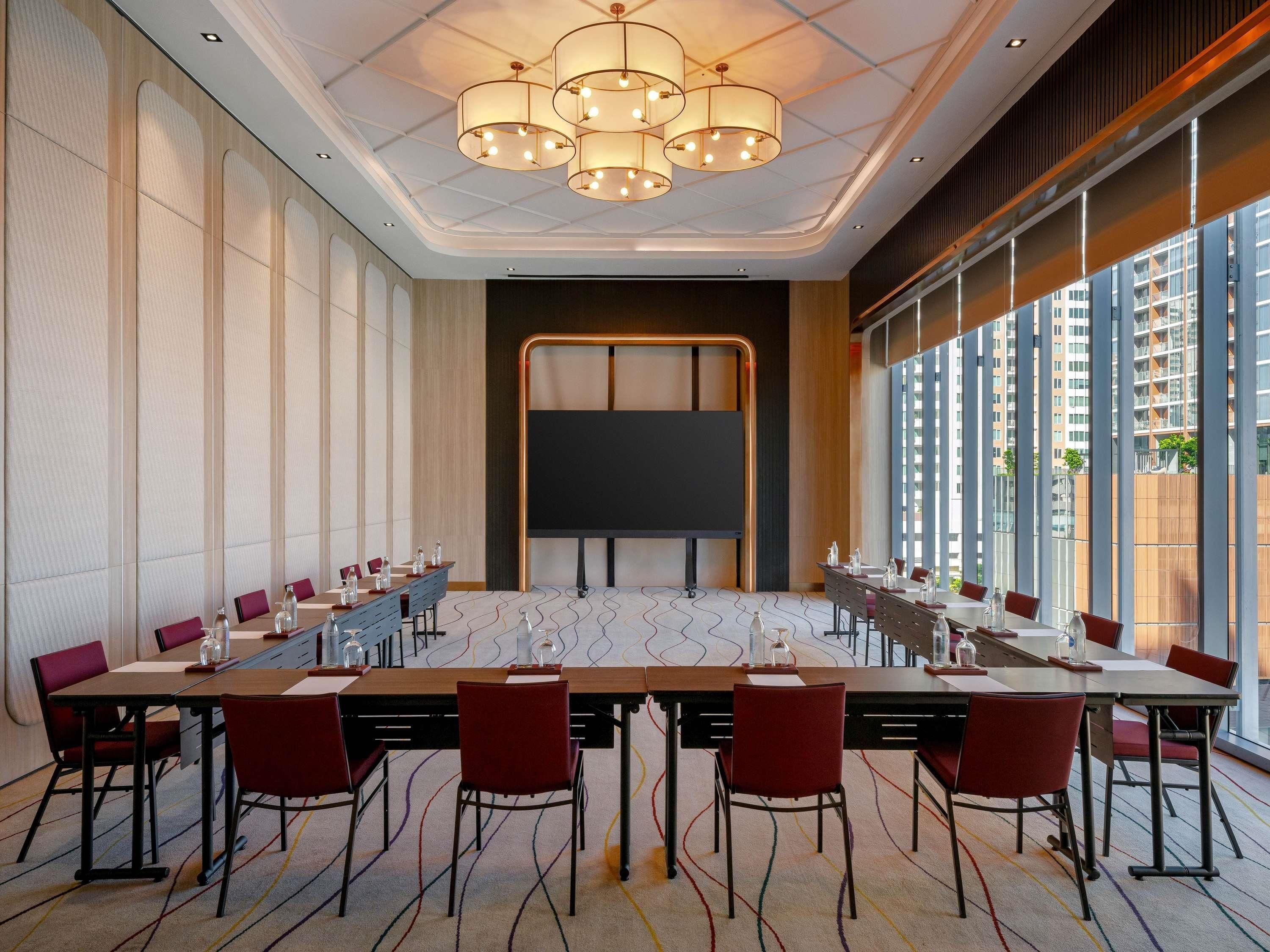 A conference room with a long table, chairs, a projector screen, and large windows.