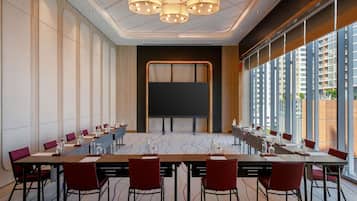 A conference room with a long table, chairs, a projector screen, and large windows.