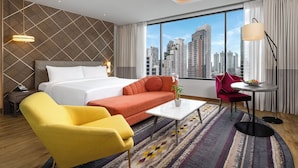 Une chambre d’hôtel avec un lit, un canapé, un fauteuil, une table basse et une vue sur le paysage urbain.