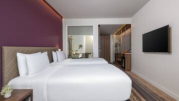 Ein Hotelzimmer mit einem großen Bett, einem Nachttisch mit einer Vase, einem Spiegel und einem an der Wand befestigten Fernseher.
