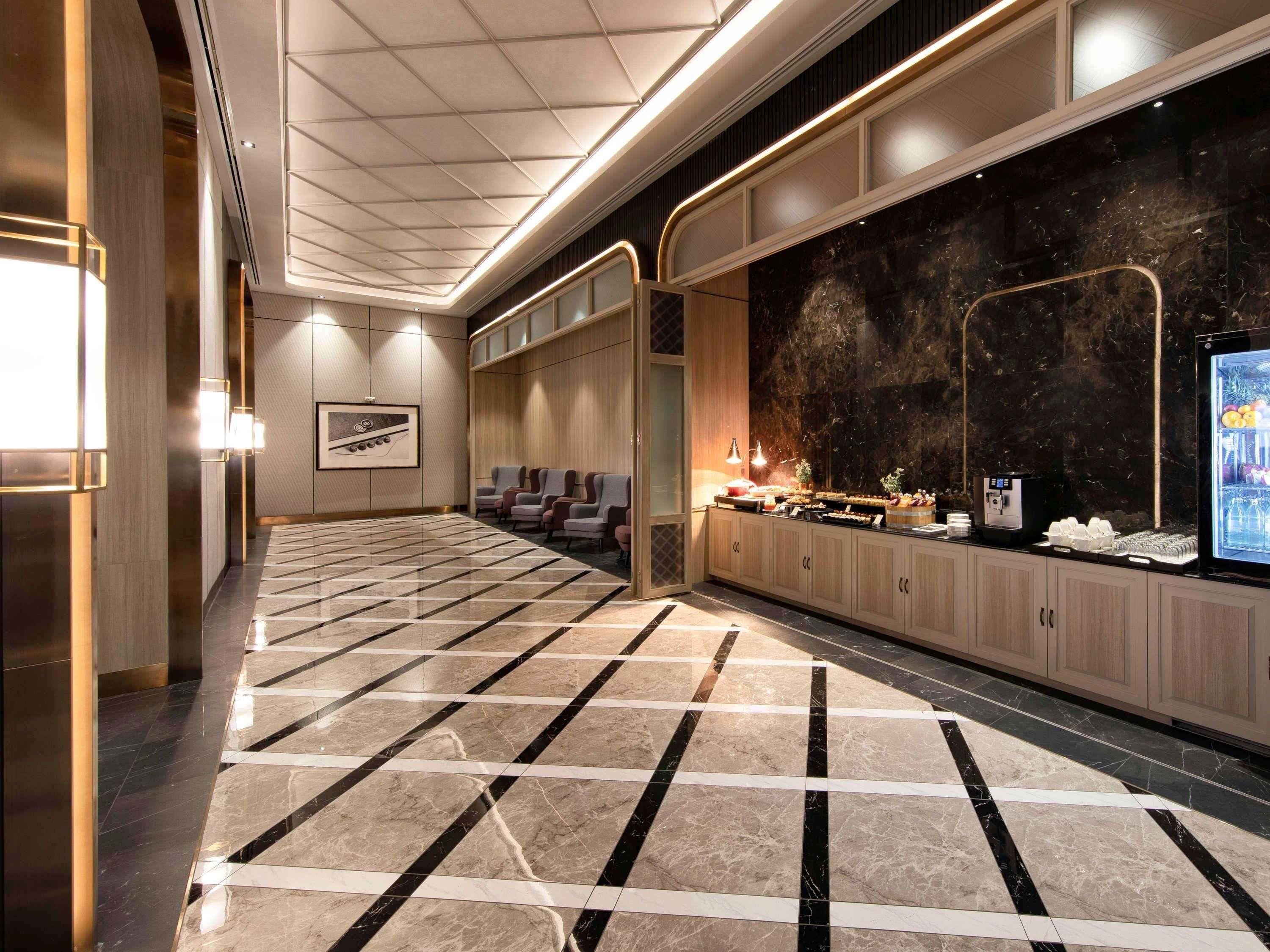 A hotel lobby with a check-in counter, seating area, and a large marble-patterned floor.