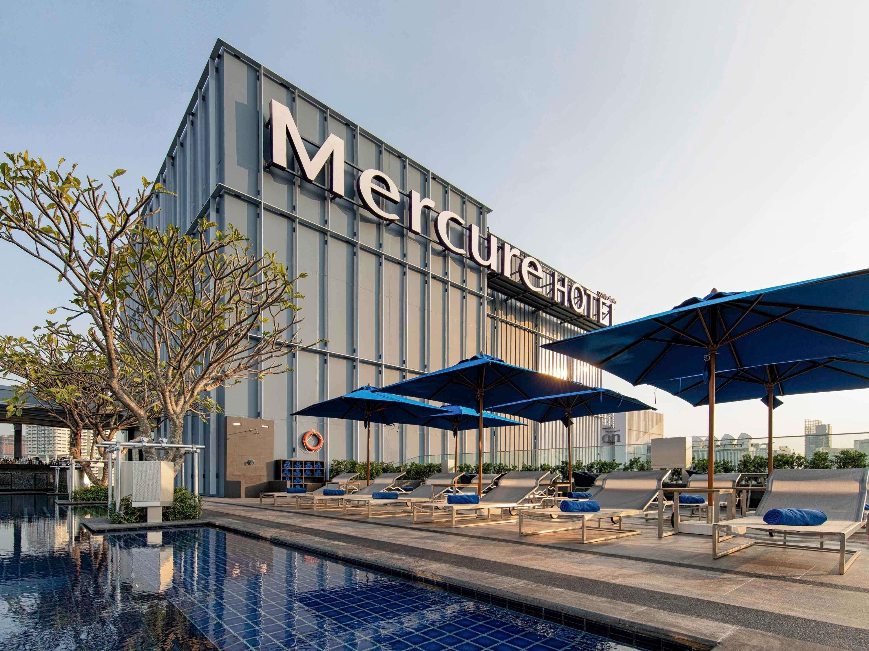 Ein Hotel namens Mercure mit Schwimmbad, Liegestühlen und Sonnenschirmen.