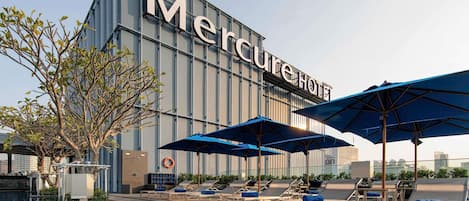 Un hotel llamado Mercure con piscina, sillones de descanso y sombrillas.