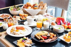 Un bufé de desayuno con diversos platos, entre ellos huevos, salchichas y pasteles.