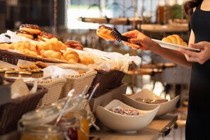 Een ontbijtbuffet met diverse gebakjes en iemand die eten opschept.