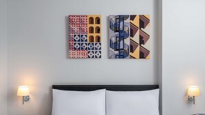 A hotel room with a bed, two bedside tables, a wall-mounted lamp, and two pieces of wall art. - Ibis Bangkok Sukhumvit 24 (Bangkok)