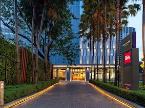 A hotel entrance with a paved pathway leading to the doors, surrounded by tall palm trees and a modern building in the background. - Ibis Bangkok Sukhumvit 24 (Bangkok)