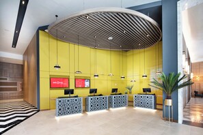 Un área de recepción con techo curvo, pared amarilla y mostrador con pantalla digital.