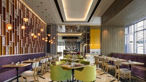 Ein modernes Restaurant mit Marmorboden, grünen und gelben Stühlen und Pendelleuchten.