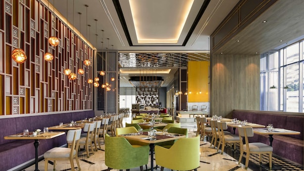 Un interior de restaurante moderno con suelo de mármol, sillas verdes y amarillas, e iluminación colgante.