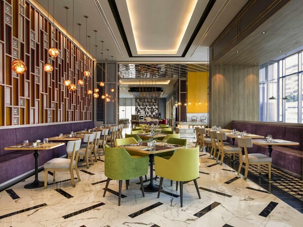 Un interior de restaurante moderno con suelo de mármol, sillas verdes y amarillas, e iluminación colgante.