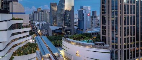 A modern hotel with a prominent glass facade, a rooftop pool, and a train station nearby.